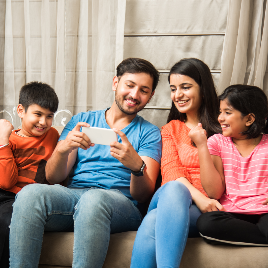 A family of four sitting on a couch and smiling together. Art-based therapy for individuals, couples and families in Melbourne – Book your session with Kathaprana now.
