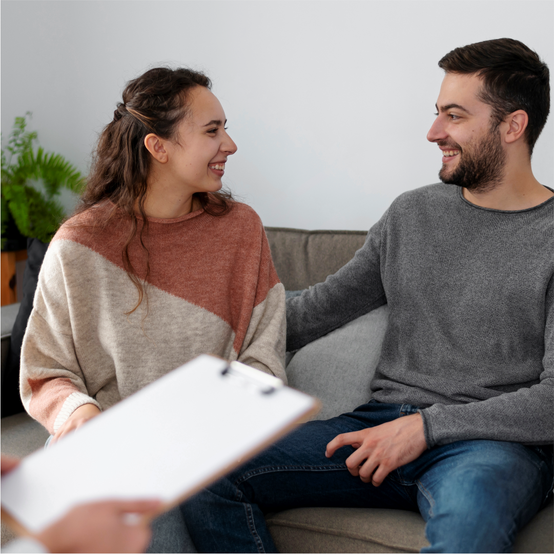 A couple sitting on a couch and smiling at each other. South Asian Couple Ttherapy center in Melbourne – Opt for healing through movement and mindfulness with Kathaprana.
