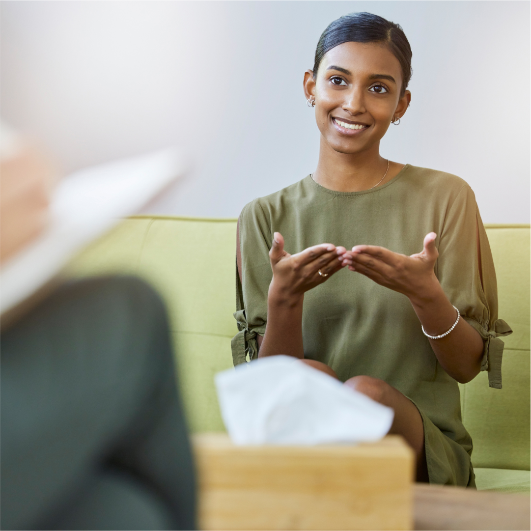 A woman sitting on a couch explaining something to her therapist. Art-based therapy for individuals, couples and families in Melbourne – Book your session with Kathaprana now.